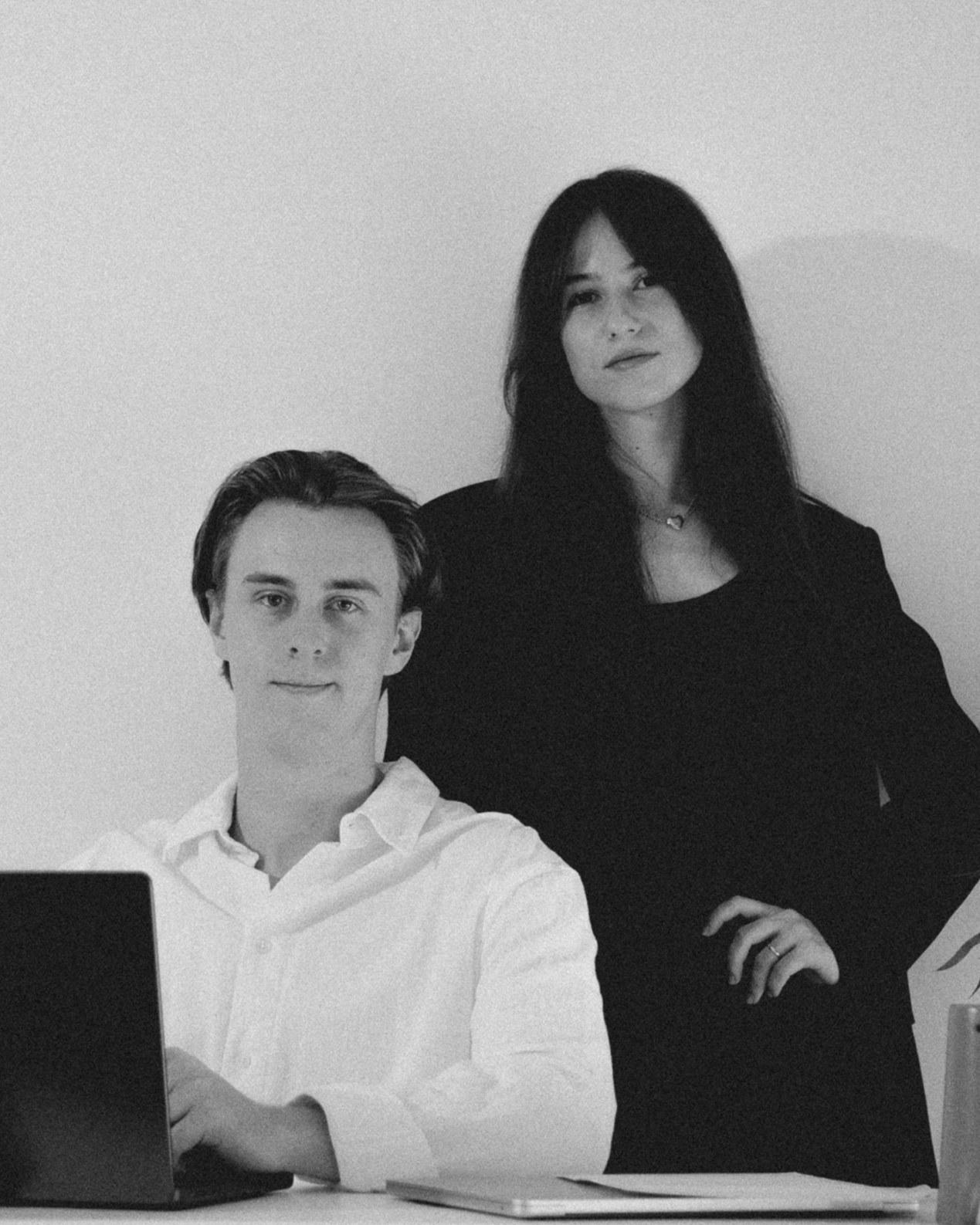 Alexandra and James, the founders of Solé, in the studio: James at a laptop, Alexandra standing beside him, black and white photograph