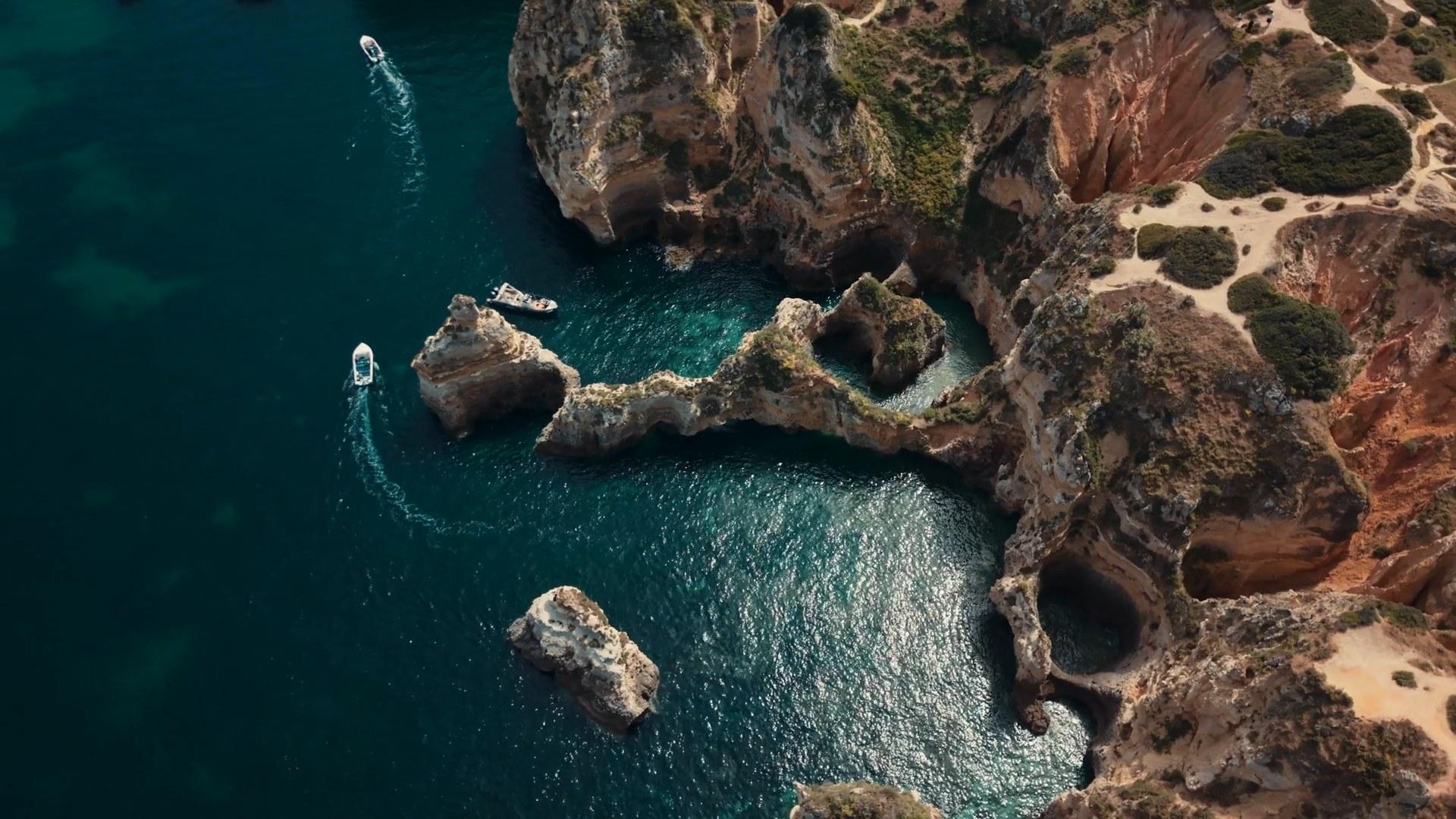Boats around limestone cliffs and sea arches, seen from above, a frame from Solé's own production reel.
